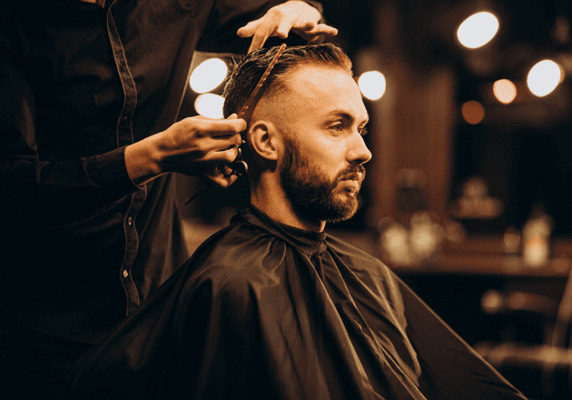 Barbier schneidet einem bärtigen Mann die Haare mit Kamm und Schere: klassischer Herrenschnitt in Mailand